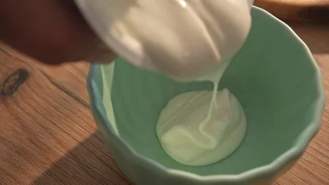 Spoon helps pour creamy white yogurt into mint-colored ceramic bowl Stock Footage 312708563