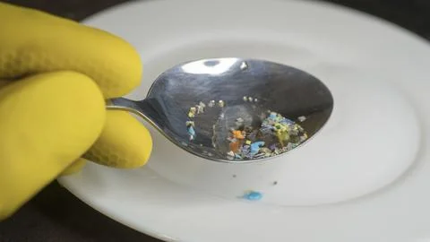 Spoon holding microplastic fragments over a white plate. 스톡 사진