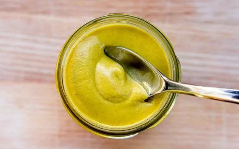 A spoon in a jar of freshly opened dijon mustard Stock Photos