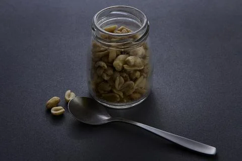 Spoon with jar of peanuts on dark surface minimalist nutrition concept Foto stock