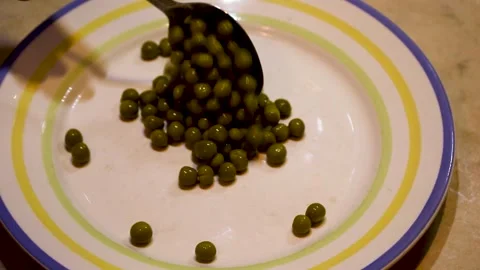 Spoon lifting green peas from an empty plate in a kitchen scene Stock Footage 341832851