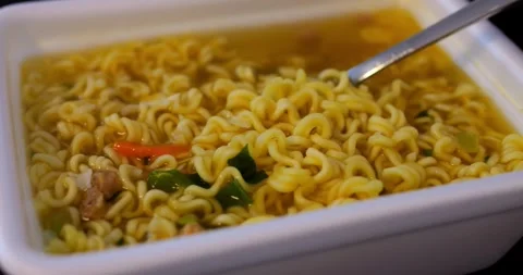 Spoon lifting noodles from white container, broth dripping, vegetables floating Stock-Footage 315692887