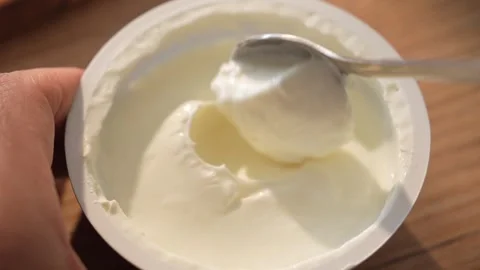 Spoon lifts thick yogurt from open cup in natural kitchen light Stock Footage 312708334