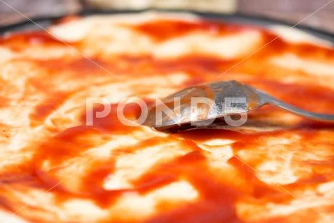 Spoon on the pizza dough coated with ketchup Stock Photos