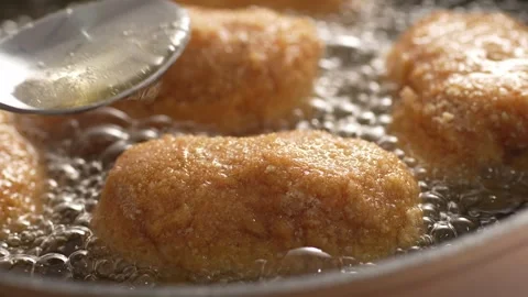 Spoon pouring boiling oil over Breaded Cutlets. Stock Footage 258651941