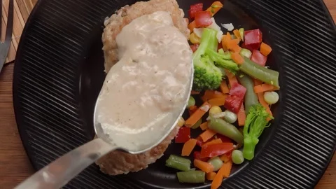 A spoon pours bechamel over meatball jn a plate Stock Footage 295657012