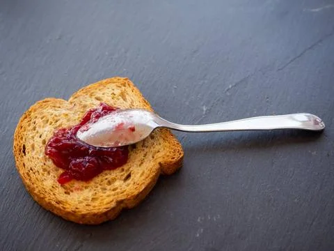  A spoon with raspberry jam on a slice of toast on a plate slate A spoon w... Stock Photos