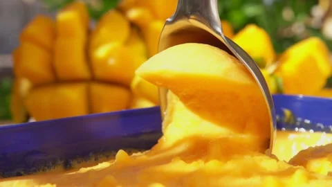 Spoon is scooping frozen mango ice-cream gelato on the background of ripe mango Stock Footage 167008754