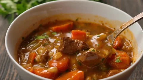 A spoon scoops up cooked pearl barley soup with beef and vegetables Stock Footage 312794624