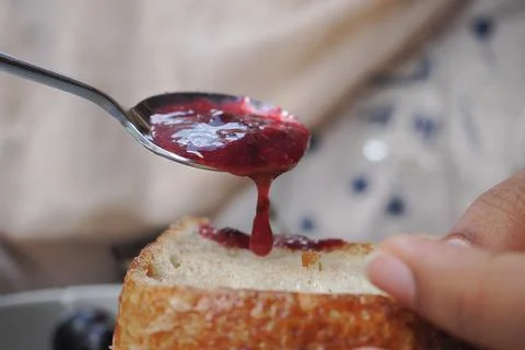 Spoon spreading berry jam on a slice of bread at breakfast Stock-Fotos