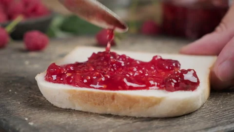 Spoon spreading raspberry jam on piece of toast Stock Footage 218462179