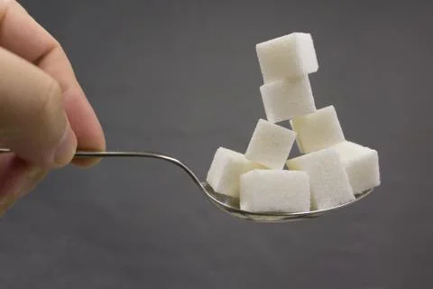 Spoon with stack of sugar cubes piled compared with cola refresh drink in swe Stockfoto's