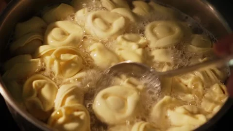 Spoon stirs boiling tortelloni inside metal pot on stovetop Stock Footage 312343917