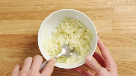 Spoon stirs diced pear in white bowl on wooden table. Video stock 344769782