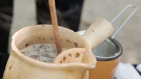 A spoon stirs the floral tea inside the pot, releasing steam and highlighting Stock-Footage 313485477