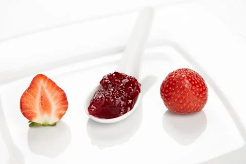 A spoon of strawberry jam and a strawberry on  a plate Stock Photos