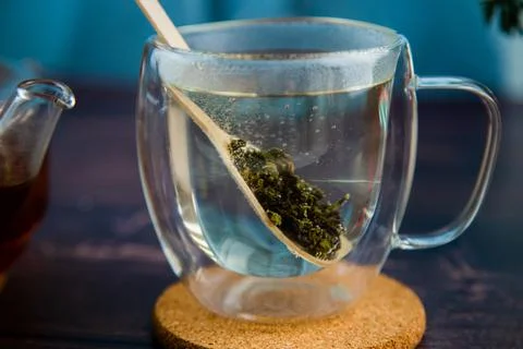 A spoon with tea was placed in a transparent mug with hot water, the tea Stock Photos