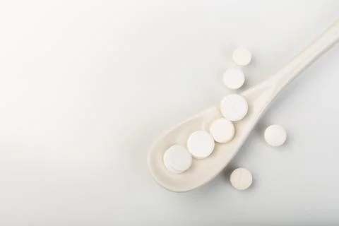 Spoon with white tablets on white background- IMAGE Stock Photos