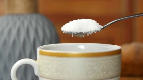 Spoonful of white sugar granules slowly falling into white cup close up mac.. Stock Footage 332407772