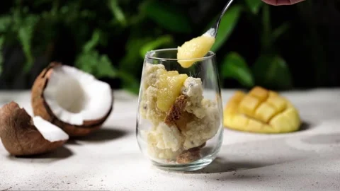 Spooning mango puree onto vegan coconut ice cream in a glass 库存影片 261558759