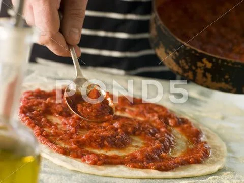 Spooning Tomato sauce onto a Pizza Base Stock Photos