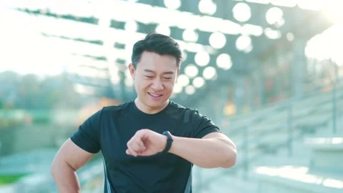 Sport asian man looking smart watch at modern track. Man runner using smartwatch Stock Footage 165677148