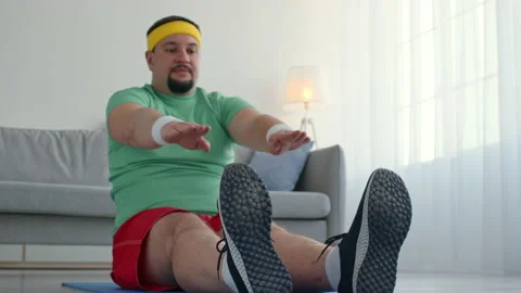 Sport beginner. Chubby man stretching at home, sitting on floor and reaching to Video stock 156264665