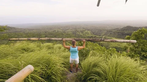 Sport man doing press exercise with heavy wooden barbell on green hill landscape Stock Footage 105326174