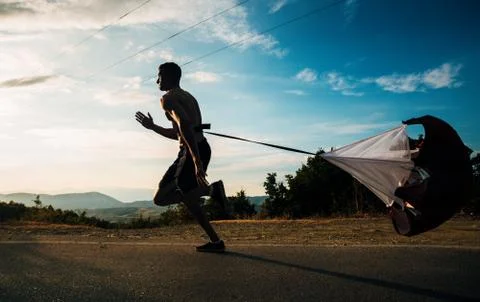 Sportive guy running fast while carrying sport parachute on mountain path aga Photos