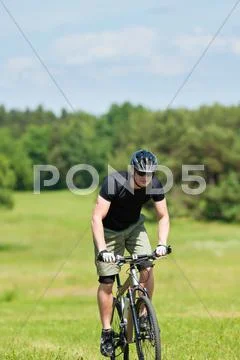Sportive man mountain biking uphill sunny meadows Stock Photos
