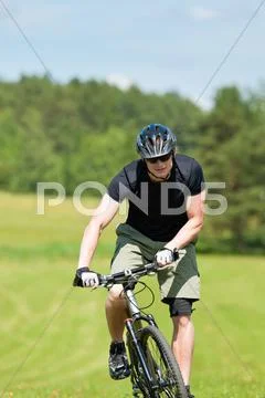 Sportive man mountain biking uphill sunny meadows Stock Photos