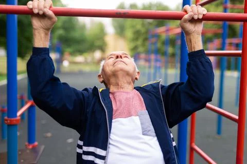 Sportive old man doing pull-ups outdoors Stock Photos