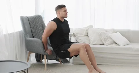 Sportive young man is doing triceps exercise near armchair at home, side view. Stock Footage 143924971