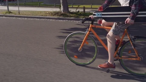A sports guy on a bicycle with a longboard under his arm rushes down the city Stock Footage