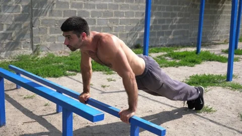 Sportsman performing dynamic push-up workout on blue parallel bars, showcasing Stock Footage 329757060