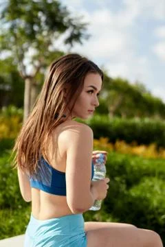 Sportswoman drinks water from plastic bottle in the park after training Stock Photos
