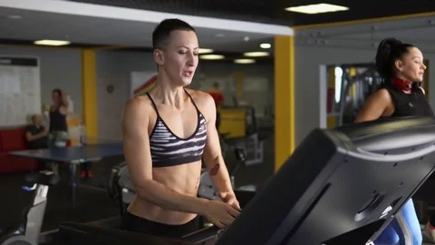 A sportswoman is intensively running on a treadmill, using hands in fitness club Stock Footage