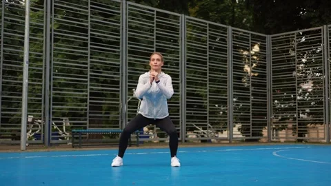Sportswoman in tracksuit making step aside and squatting on court outdoors Video stock 252194403