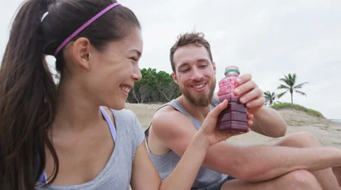 Sporty active couple sharing beet juice on beach relaxing after workout Stock Footage 61746184