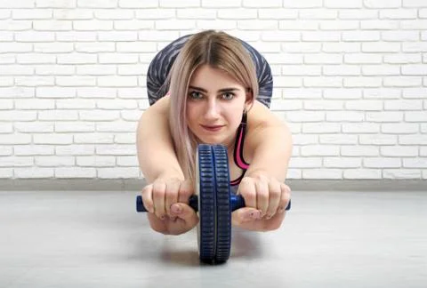 Sporty blonde girl performs exercises with a wheel for the press Photos
