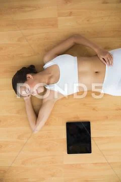 Sporty brunette with closed eyes lying next to a tablet Stock Photos