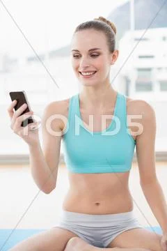 Sporty cheerful woman holding phone while sitting on exercising mat Stock Photos
