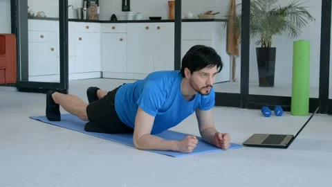 Sporty fit man watching tutorial video on laptop, doing yoga plank 스톡 동영상 330930964