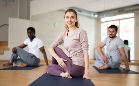 Sporty girl practicing Matsyendrasana during group yoga training Stock Photos