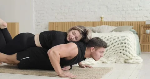 Sporty man doing push up exercises at home with woman lying above on his back. Stock Footage 146679678