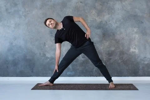 Sporty young man practicing yoga, doing stretching exercise, extended triangle Stock Photos