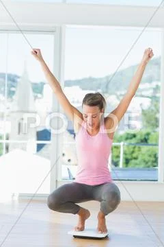 Sporty young woman crouching on weighing scale in gym Stock Photos