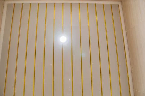 Spot ceiling lamp on the ceiling made of plastic panels with gold slats Stock Photos