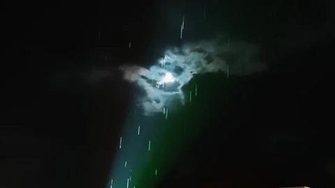 Spotlight beam and rain drops lit by moon through clouds at night Stock Footage 336092449