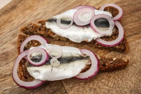 Sprat on a piece of black bread. Fish with bread and red onion on a cutting t Stock Photos